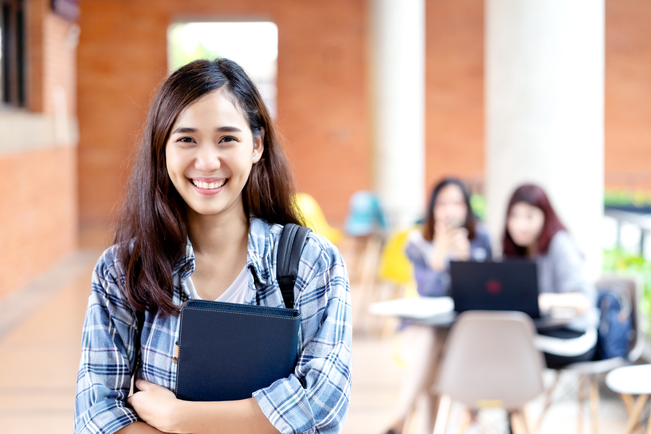 Headshot of young happy attractive asian student smiling and looking at camera with friends on outdoor university background. Asian woman in self future education or personalized learning concept.